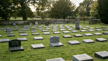 Rows of flat gravestones in a grassy cemetery with trees and a stone wall